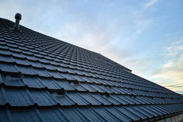 Snow guard for safety in winter on house roof top covered with ceramic shingles. Tiled covering of building.